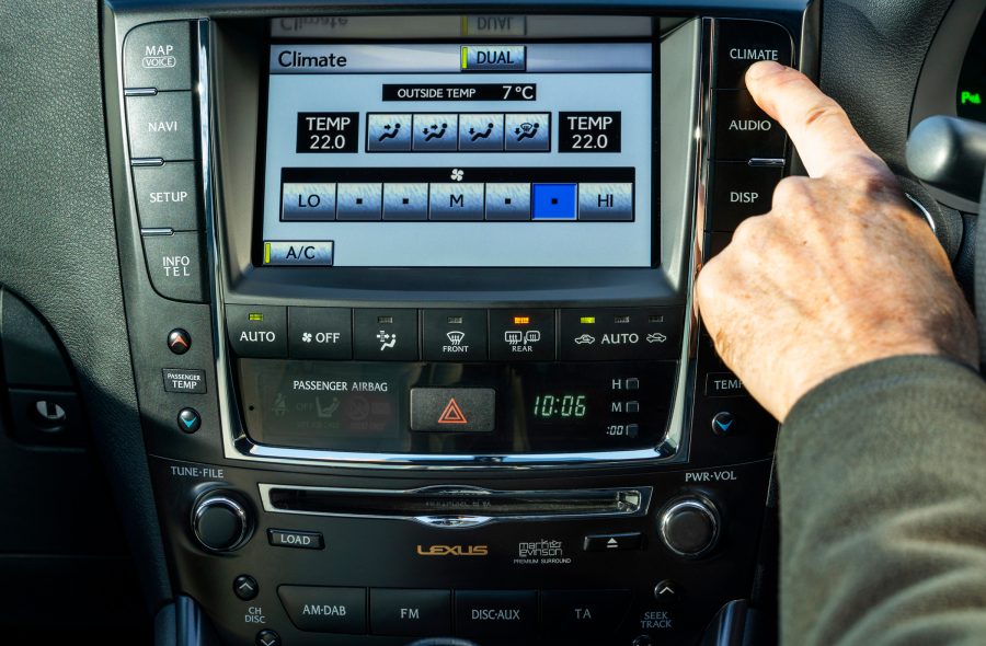 A man's hand presses the button to access climate controls on a Lexus.